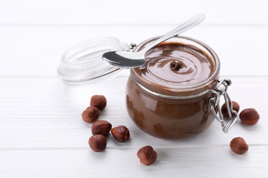 Photo of Jar with delicious chocolate paste and nuts on white wooden table