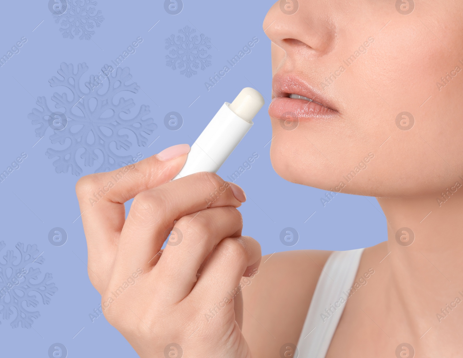 Image of Winter skin care. Woman applying lip balm, closeup. Snowflakes on pale purple background