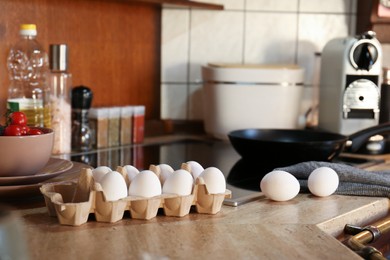 Many fresh eggs in carton and tomatoes on wooden table in kitchen. Ingredients for breakfast