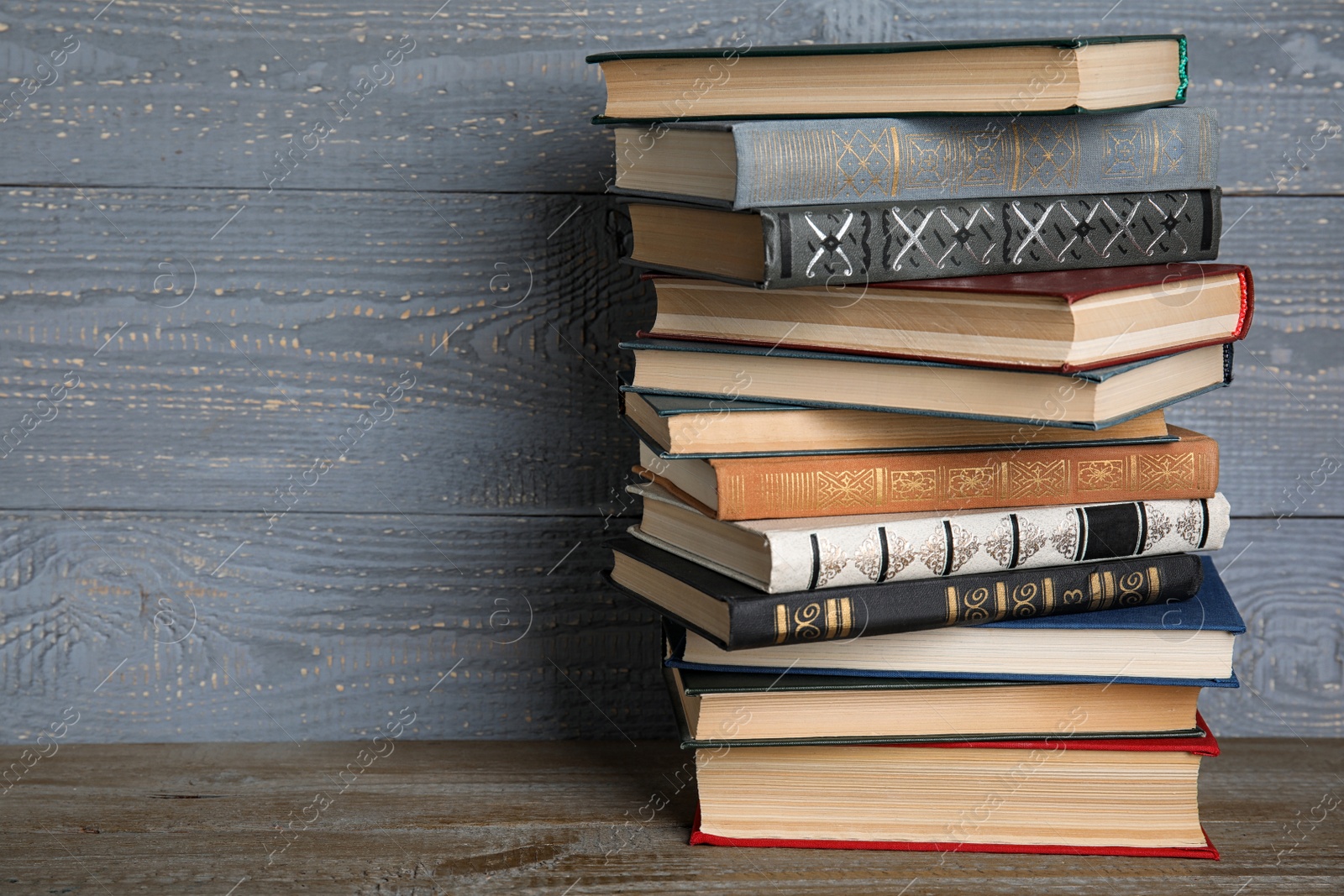 Photo of Stack of hardcover books on wooden table against grey background. Space for text