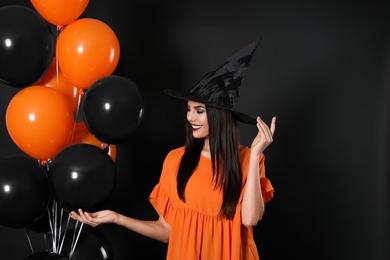 Photo of Beautiful woman wearing witch costume with balloons for Halloween party on black background