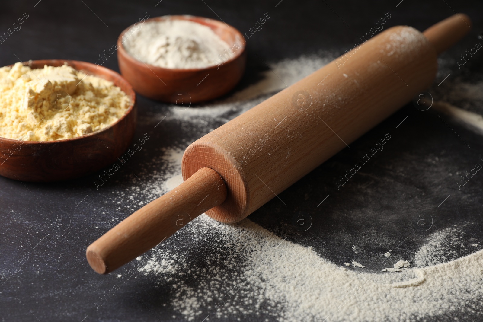 Photo of Scattered flour, rolling pin and sieve on black table, closeup