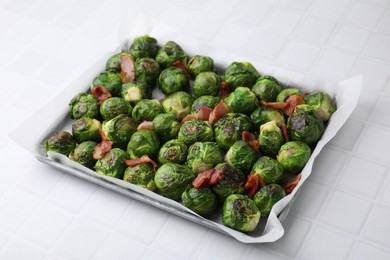 Photo of Delicious roasted Brussels sprouts and bacon in baking dish on white tiled table