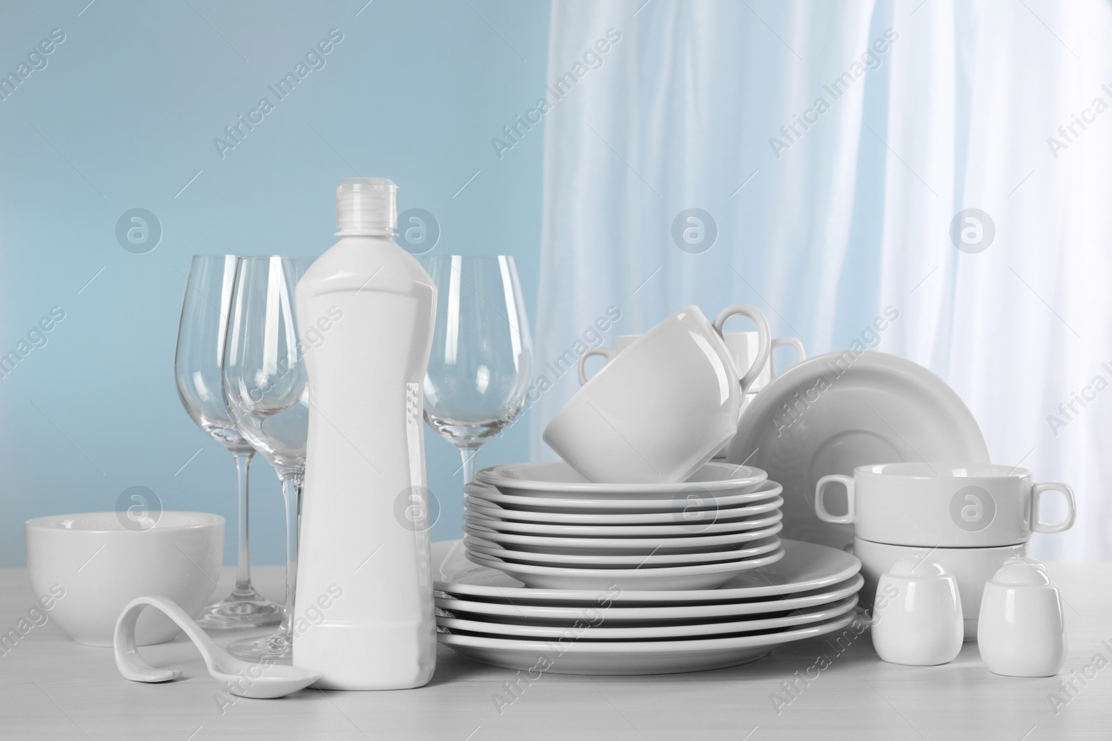 Photo of Clean dishware and bottle of detergent on light grey table