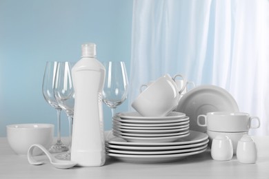 Clean dishware and bottle of detergent on light grey table