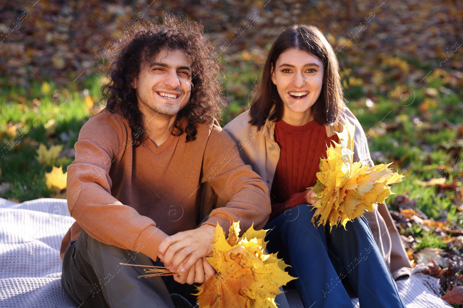 Photo of Happy young couple with dry leaves spending time together in autumn park. Dating agency