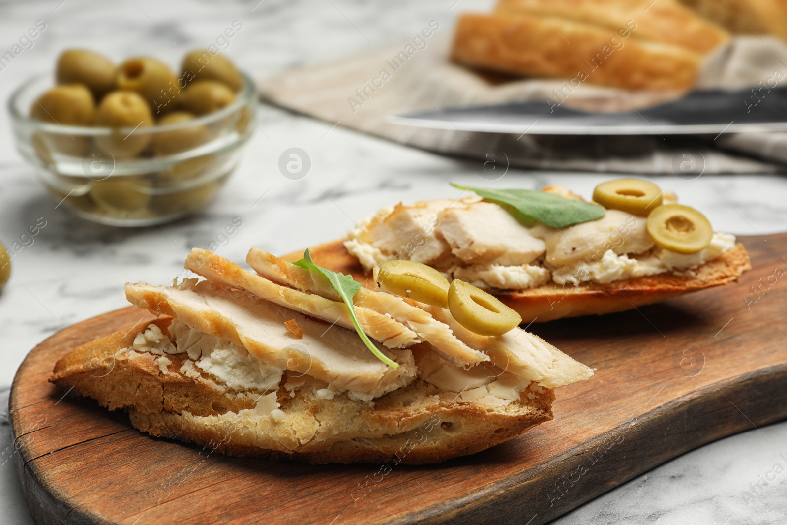 Photo of Board with delicious chicken bruschettas on white marble table