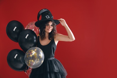 Photo of Beautiful woman in witch costume with balloons on red background, space for text. Halloween party