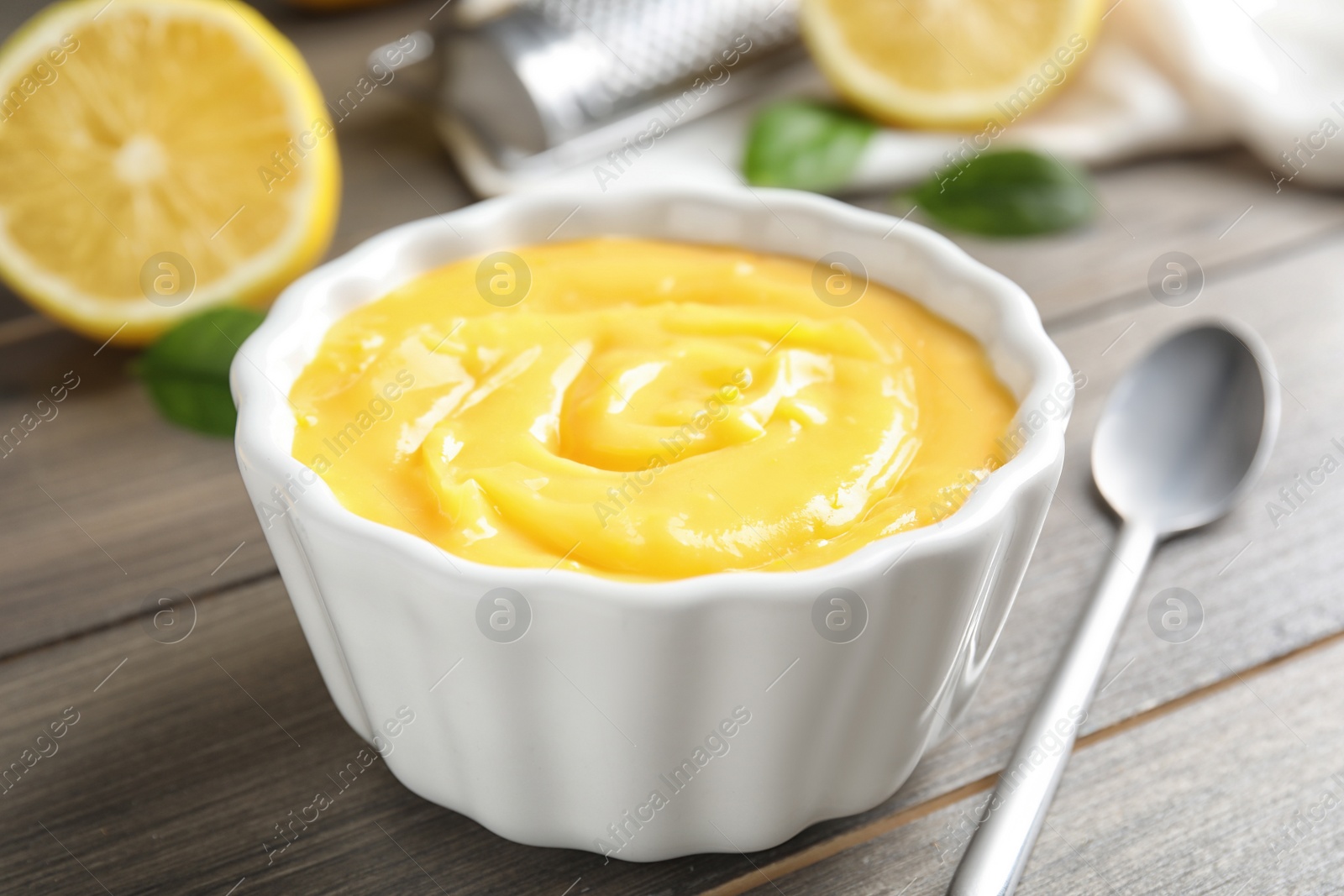 Photo of Delicious lemon curd in bowl on wooden table, closeup