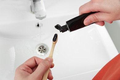 Photo of Man applying charcoal toothpaste onto toothbrush in bathroom, closeup