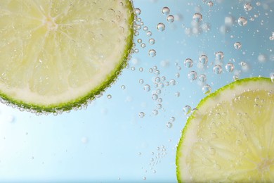 Photo of Juicy lime slices in soda water against light blue background, closeup