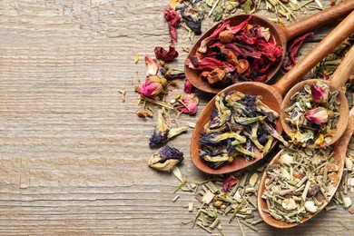 Photo of Spoons with different teas on wooden table, flat lay. Space for text