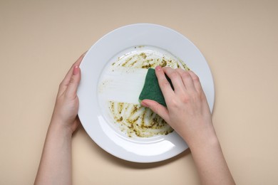 Woman washing dirty plate with sponge on beige background, top view