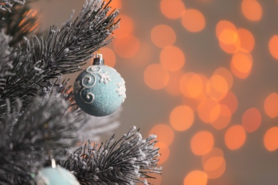 Photo of Light blue holiday bauble hanging on Christmas tree against blurred festive lights, closeup. Space for text