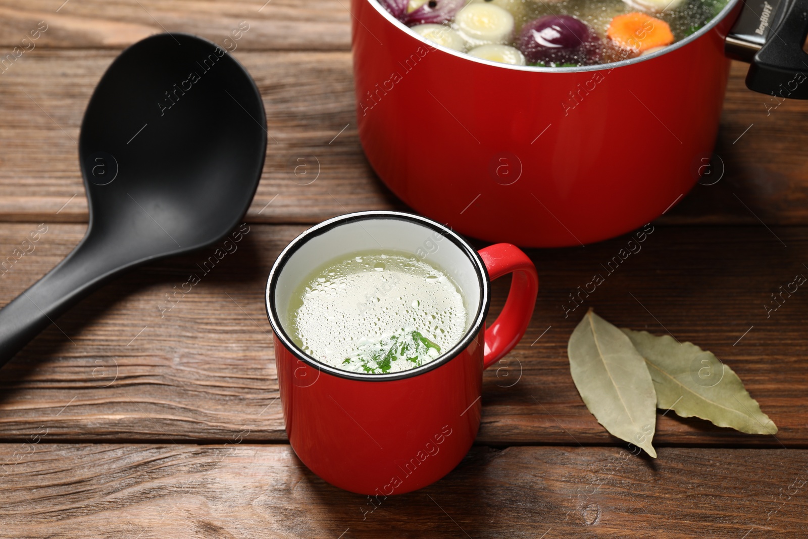 Photo of Red mug with tasty bouillon on wooden table