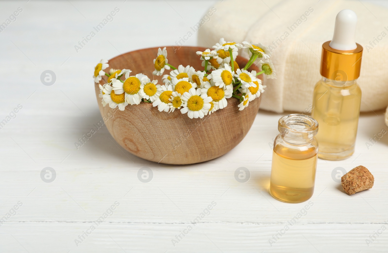 Photo of Bottles of essential oil and chamomiles on white wooden table