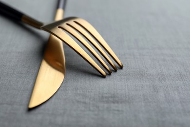 Photo of Golden fork and knife on grey table, closeup. Space for text