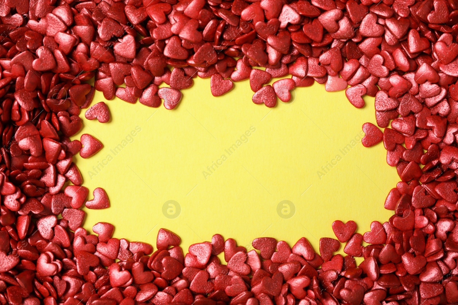 Photo of Frame made of bright heart shaped sprinkles on yellow background, flat lay. Space for text