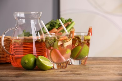 Photo of Glasses and jug of tasty rhubarb cocktail with lime fruits on wooden table, space for text