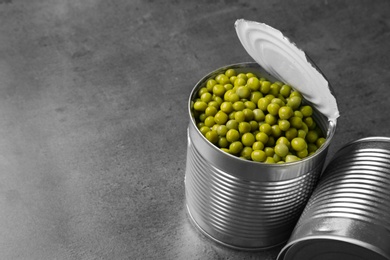 Photo of Tin cans and green peas on grey table, space for text