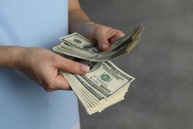 Money exchange. Woman counting dollar banknotes on grey background, closeup