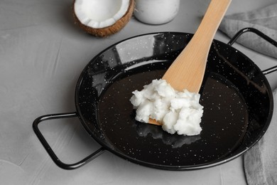Photo of Frying pan with coconut oil and wooden spatula on light grey table