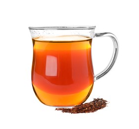 Aromatic rooibos tea in glass cup and scattered dry leaves on white background