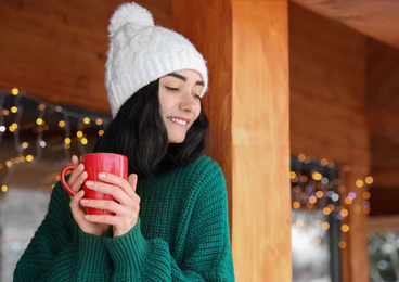 Photo of Pretty woman wearing sweater with cup near wooden terrace in winter