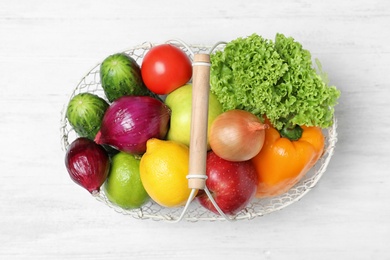 Photo of Basket with ripe fruits and vegetables on white wooden table, top view
