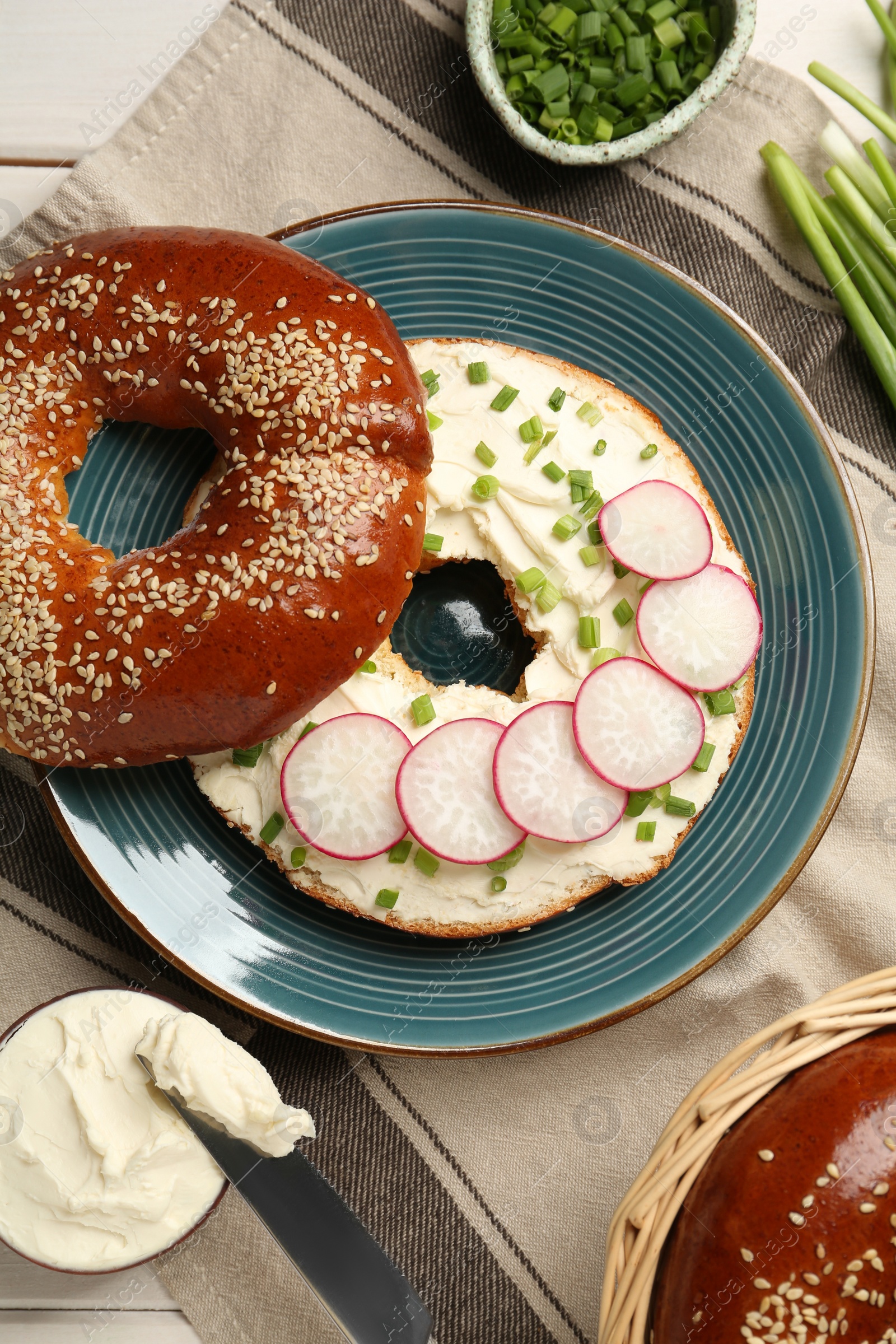 Photo of Delicious bagel with cream cheese, green onion and radish on table, flat lay