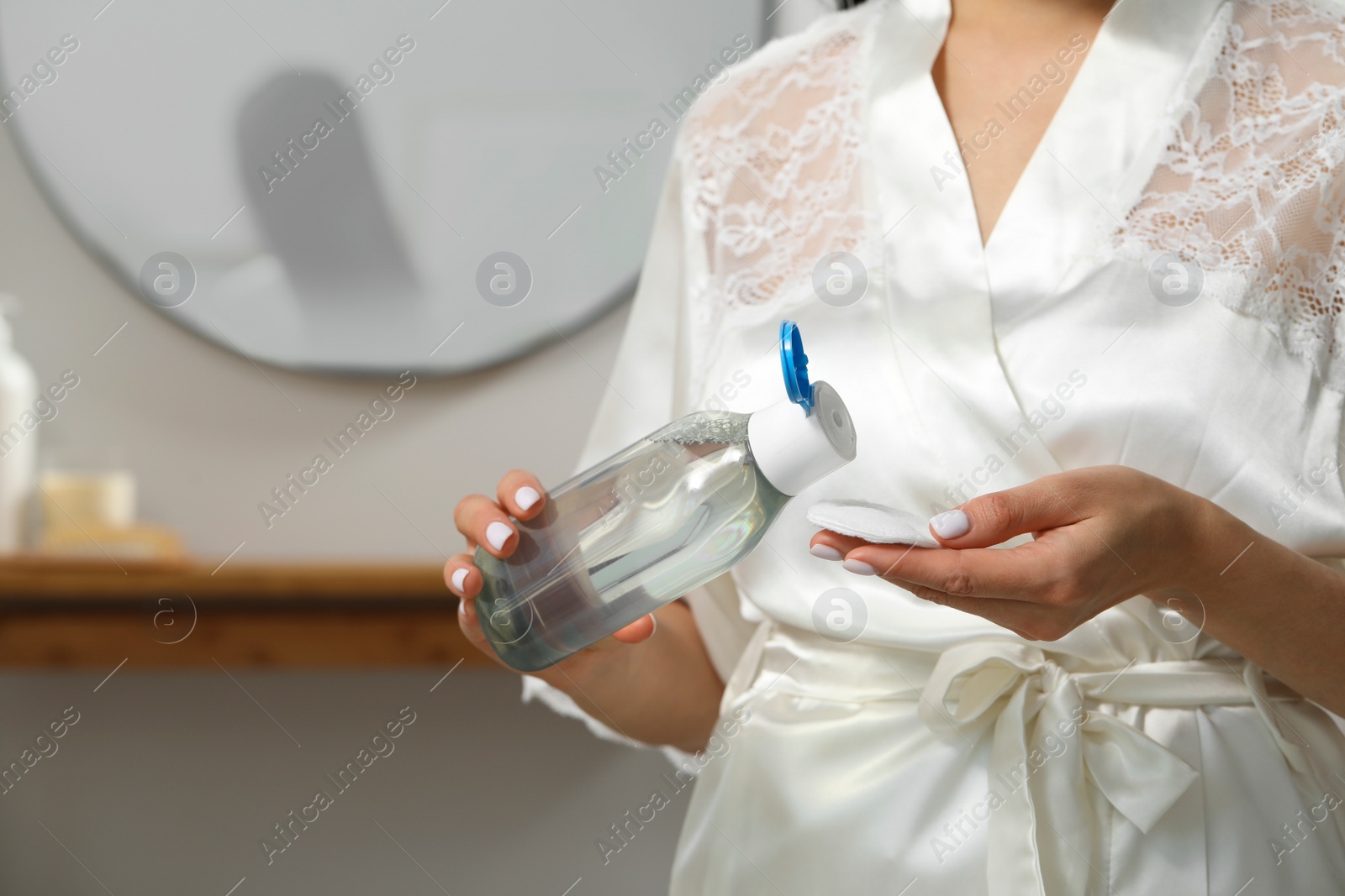 Photo of Woman pouring micellar water onto cotton pad indoors, closeup