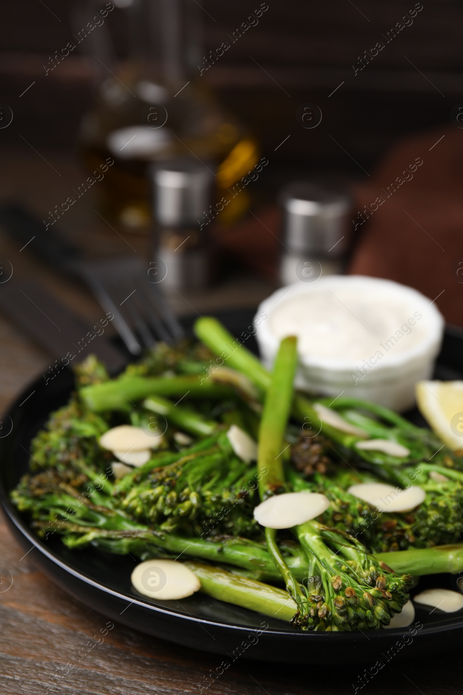 Photo of Tasty cooked broccolini with almonds and sauce on wooden table, closeup