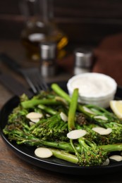 Tasty cooked broccolini with almonds and sauce on wooden table, closeup