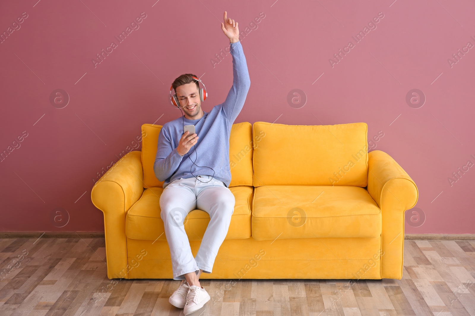 Photo of Handsome young man sitting on sofa and listening to music, indoors