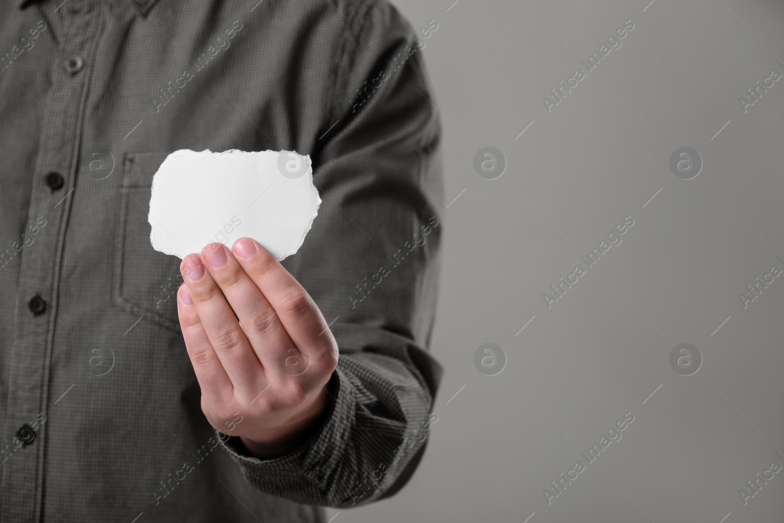 Photo of Man holding sheet of torn paper on grey background, closeup. Mockup for design