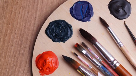 Photo of Artist's palette with many colorful paints and brushes on wooden table, top view