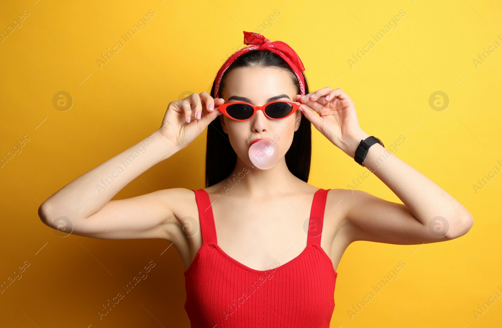 Photo of Fashionable young woman in pin up outfit blowing bubblegum on yellow background