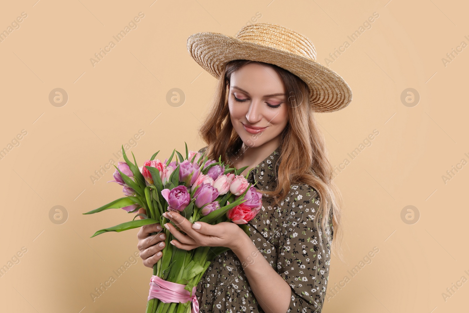 Photo of Happy young woman in straw hat holding bouquet of beautiful tulips on beige background