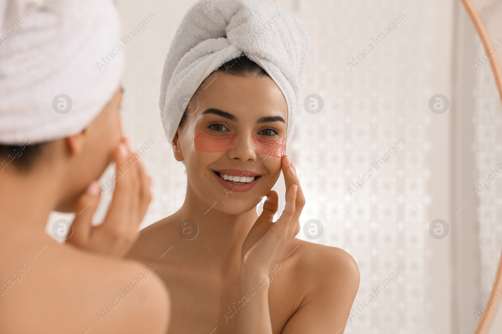 Photo of Beautiful young woman with under eye patches near mirror at home