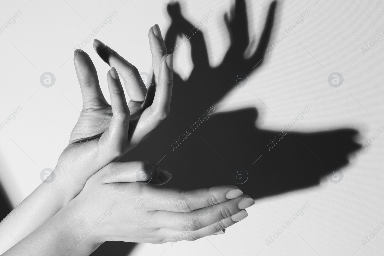 Photo of Shadow puppet. Woman making hand gesture like deer on light background, closeup. Black and white effect