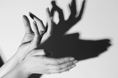 Shadow puppet. Woman making hand gesture like deer on light background, closeup. Black and white effect