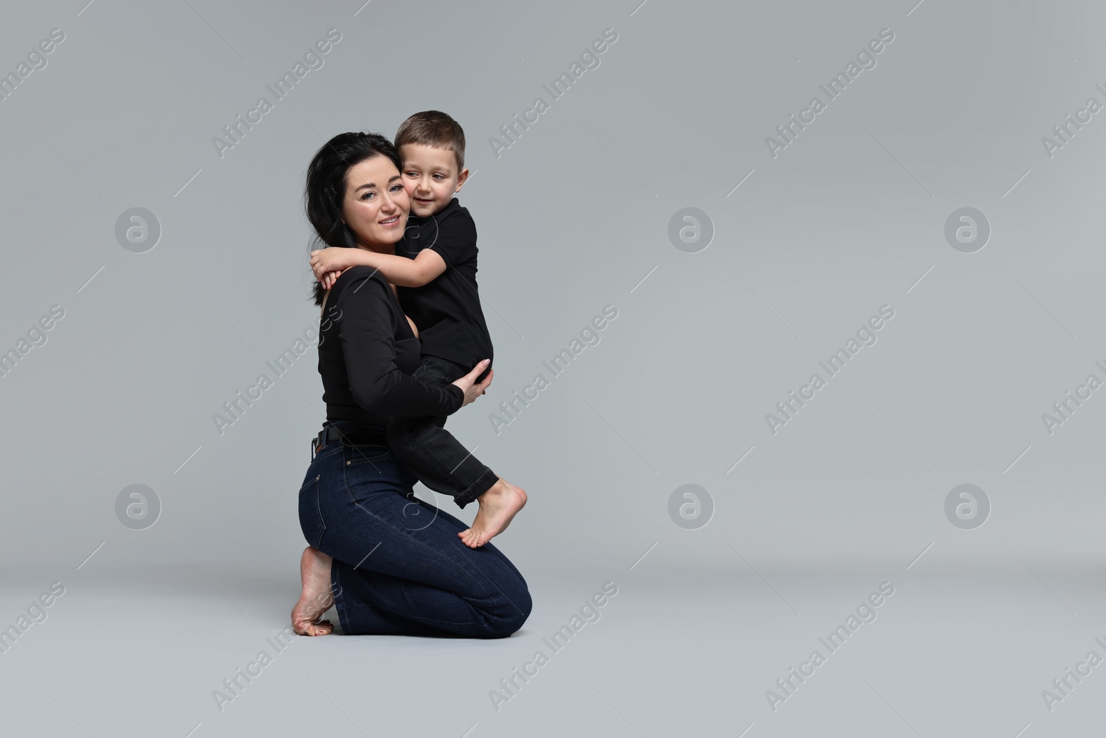 Photo of Beautiful mother hugging little son on grey background. Space for text