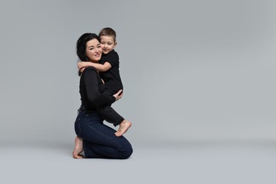 Photo of Beautiful mother hugging little son on grey background. Space for text