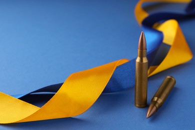 Photo of Ribbons in colors of national Ukrainian flag and bullets on blue background, closeup. Space for text