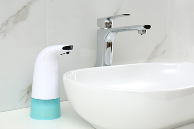 Photo of Modern automatic soap dispenser near sink in bathroom, closeup