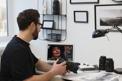 Professional photographer in glasses holding digital camera at table in office