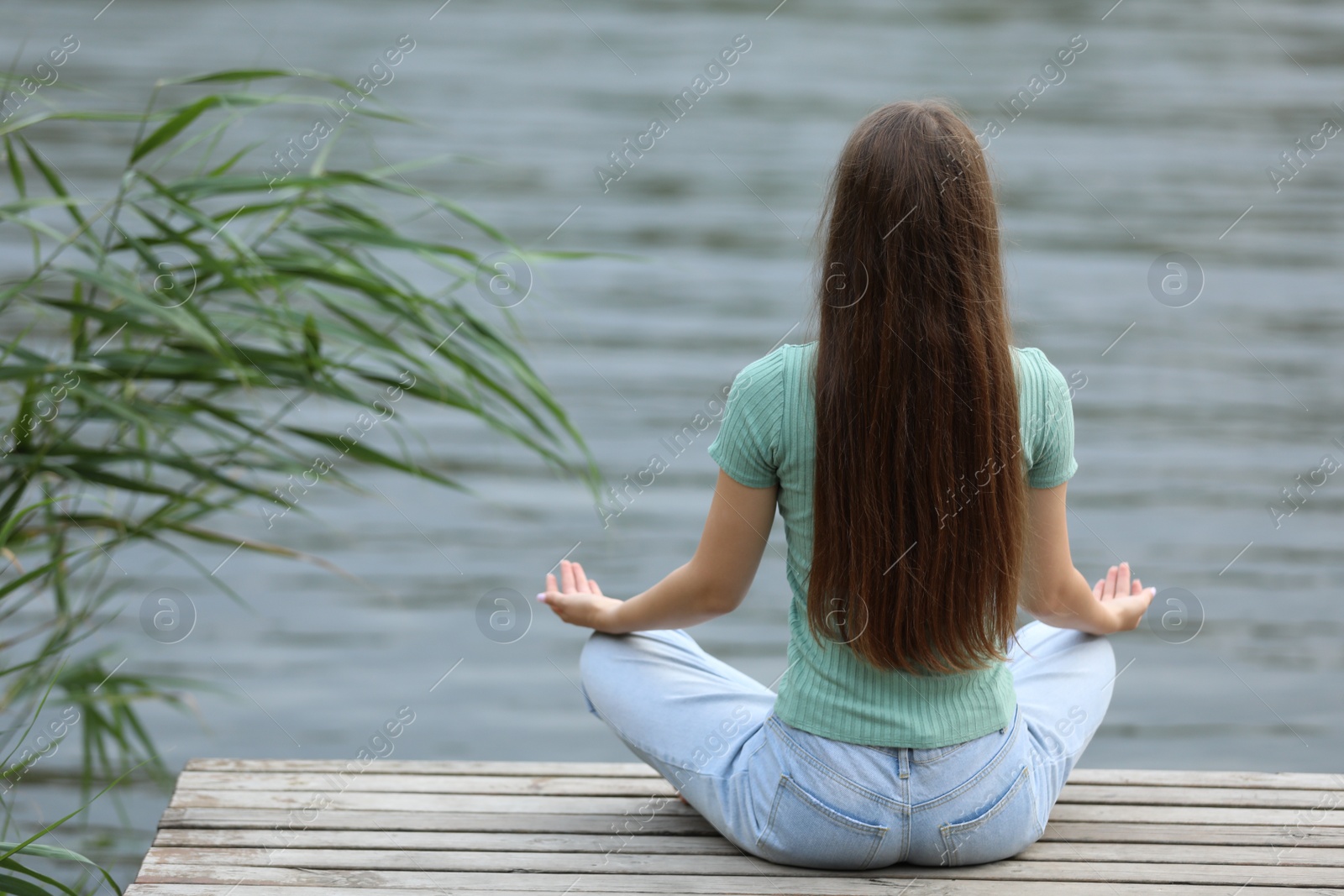 Photo of Teenage girl meditating near river, back view