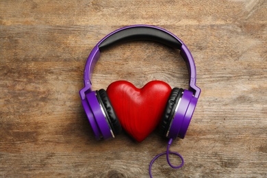 Photo of Decorative heart with modern headphones on wooden background, top view