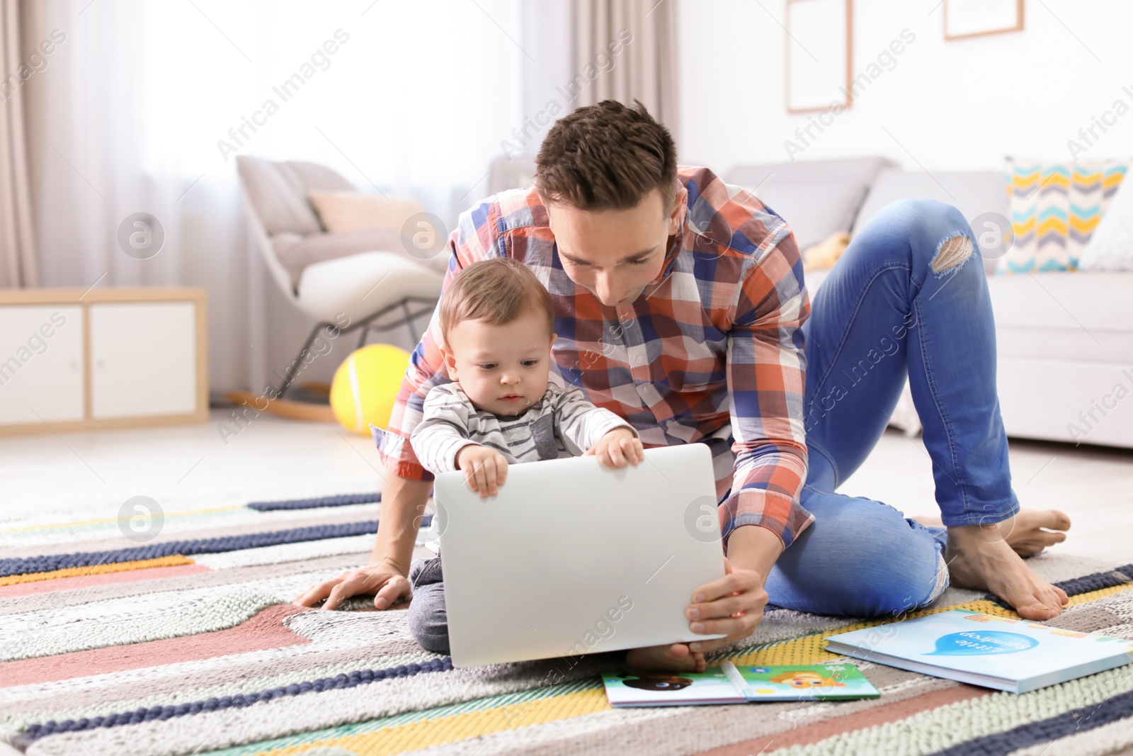 Photo of Young father with his cute little son using laptop at home