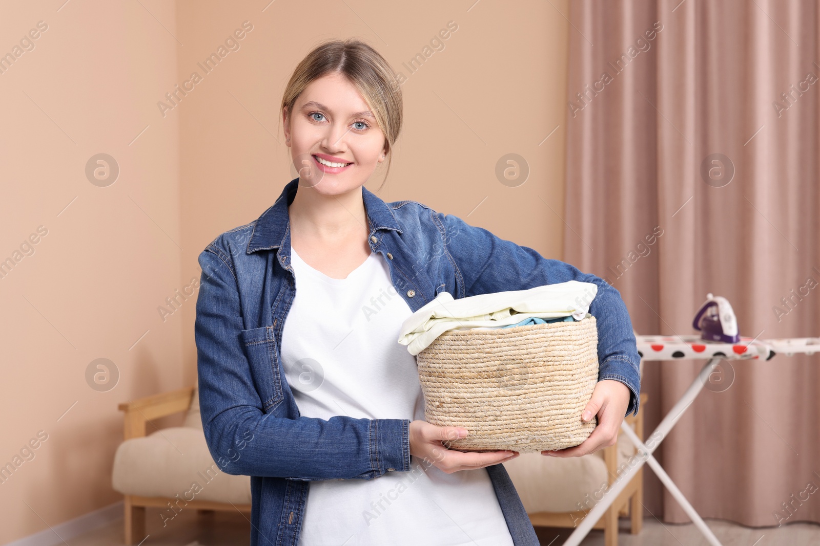 Photo of Happy woman with basket full of laundry at home